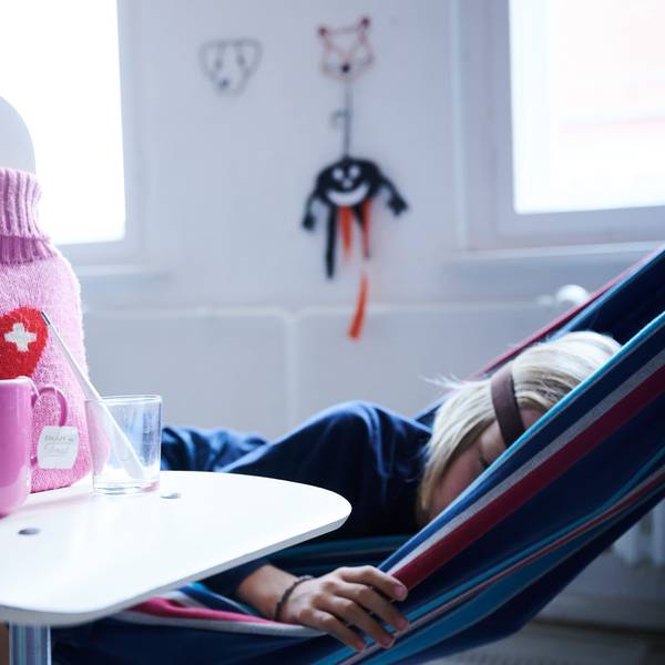 ARCHIV - 11.09.2021, Berlin: ILLUSTRATION - Fieberthermometer, Hustensaft, Wärmflasche und eine Tasse Tee stehen auf einem Stuhl, während ein Kind im Hintergrund in einer Hängematte liegt. In Deutschland hat nach Einschätzung des Robert Koch-Instituts (RKI) die Welle der RSV-bedingten Atemwegserkrankungen begonnen. (zu dpa «Atemwegserkrankungen: RSV-Welle in Deutschland hat laut RKI begonnen») Foto: Annette Riedl/dpa +++ dpa-Bildfunk +++