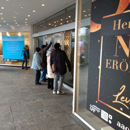 Passanten stehen vor dem geschlossenen ehemaligen Kaufhof und schauen durch die Schaufensterscheibe.