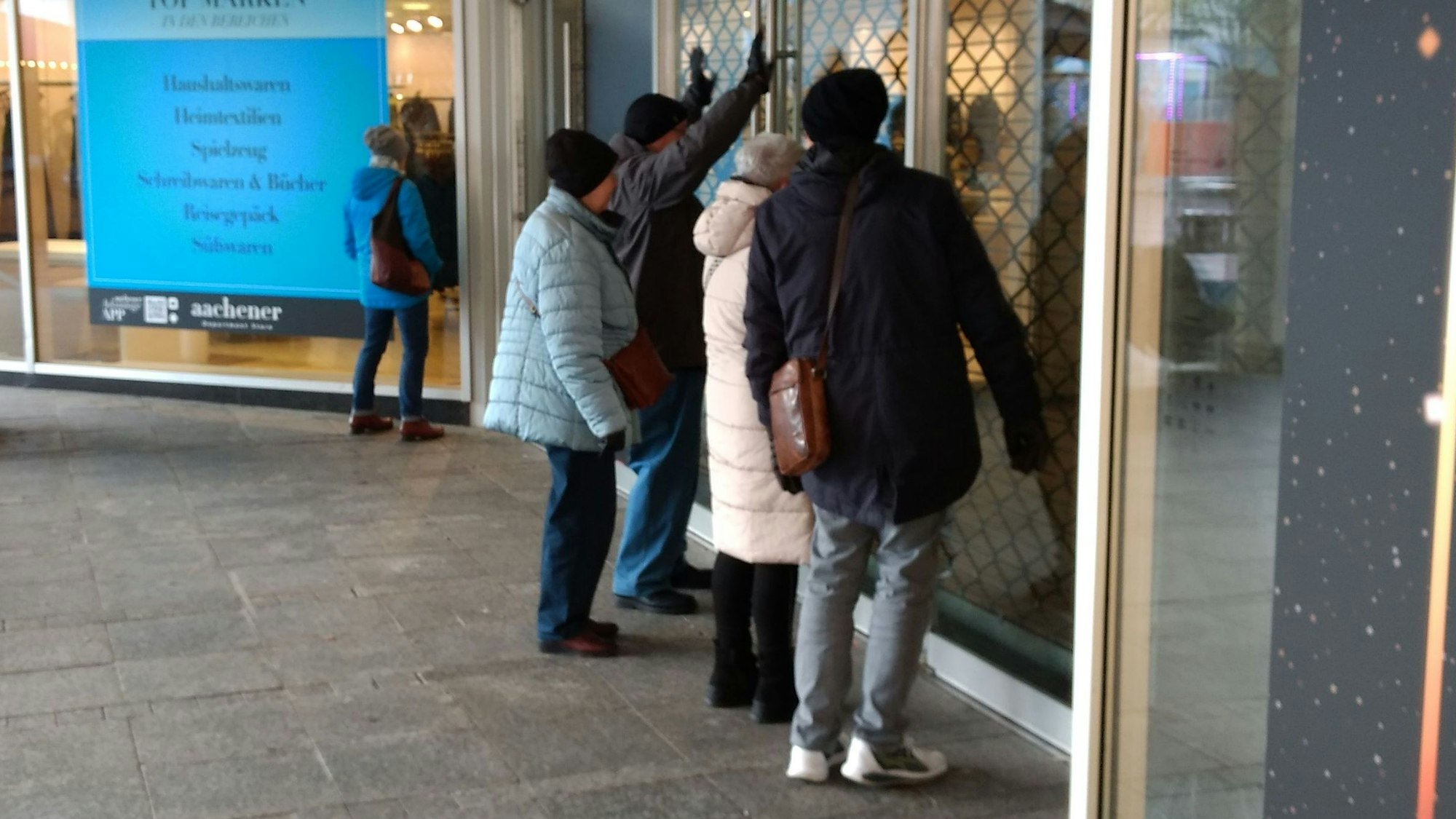 Passanten stehen vor dem geschlossenen ehemaligen Kaufhof und schauen durch die Schaufensterscheibe.