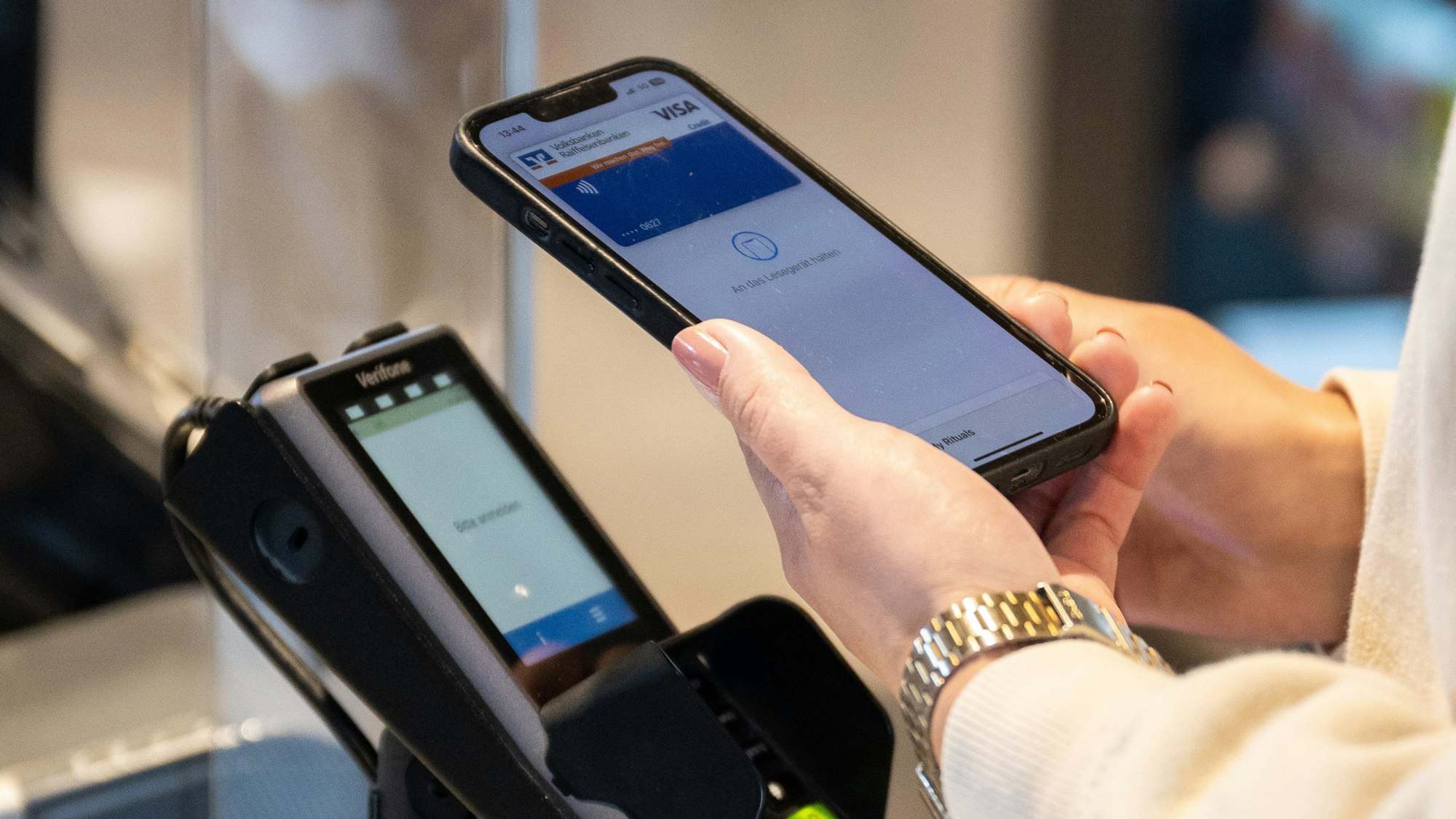 Eine Frau hält ein Smartphone zum Bezahlen an einen Scanner.