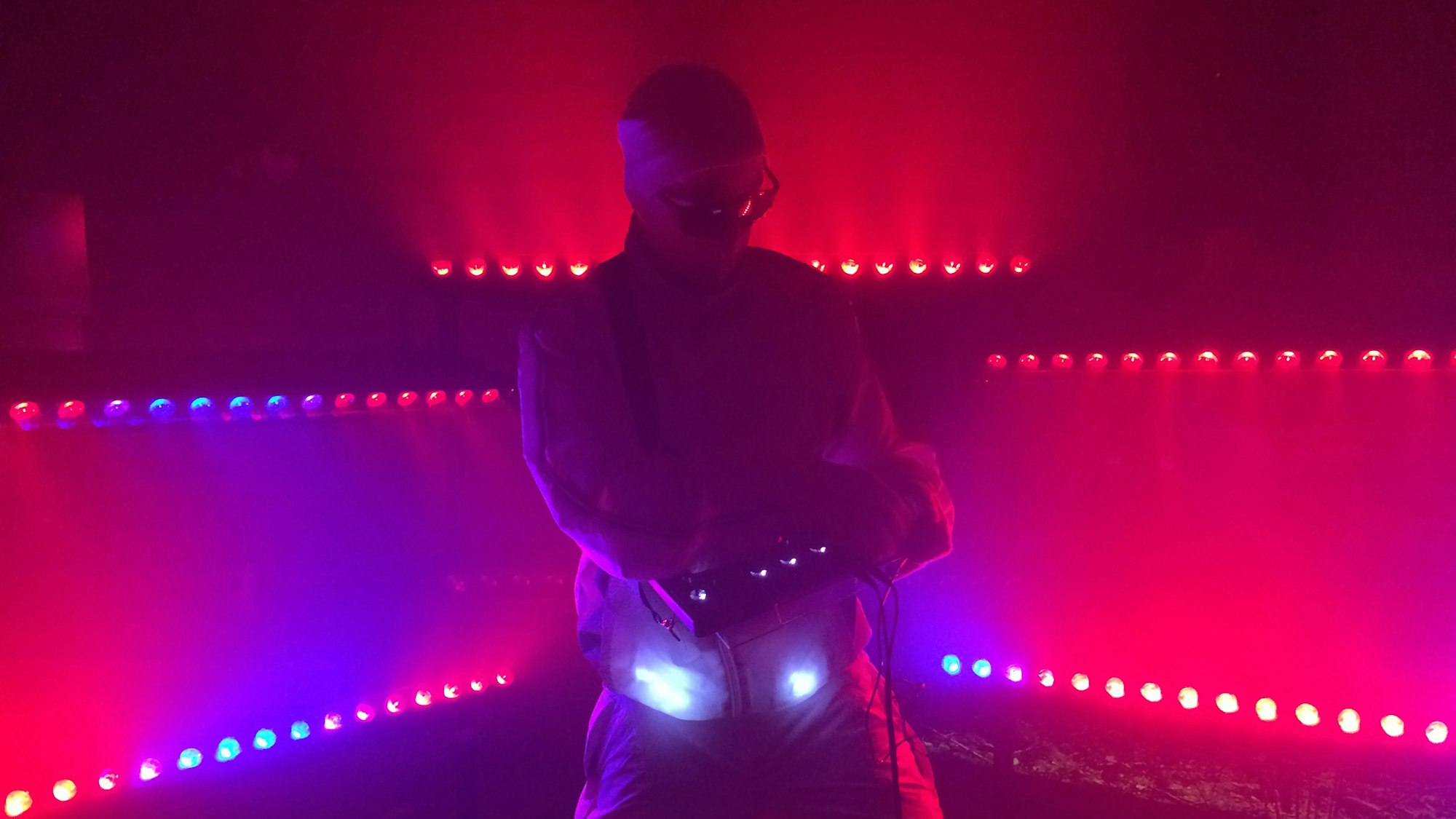 Ein Mensch steht auf der Tanzfläche, Diskobeleuchtung, er bedient ein Gerät und erzeugt vermutlich Töne damit.