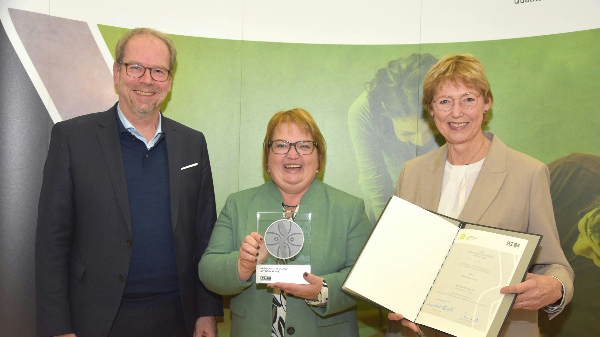 Astrid Machuj hält den Rheinlandtaler, links neben ihr steht Bürgermeister Volker Mießeler, rechts Karin Schmitt-Promny vom LVR.