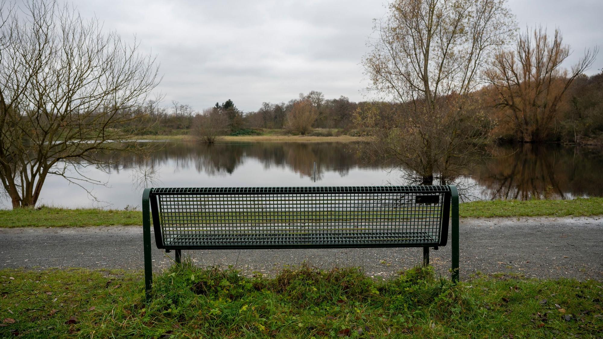 Zu sehen ist eine Parkbank vor einem Weiher.