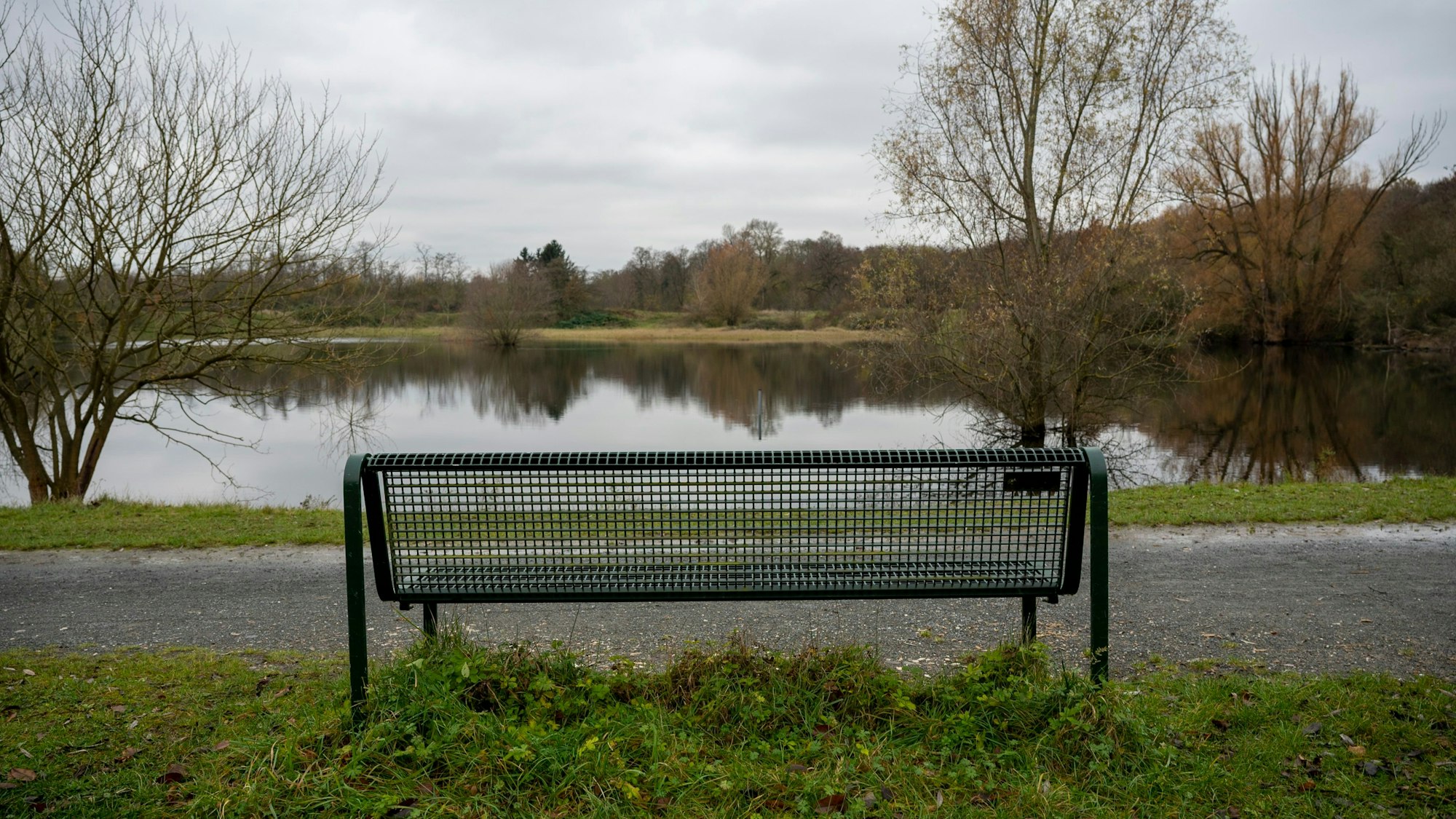 Zu sehen ist eine Parkbank vor einem Weiher.