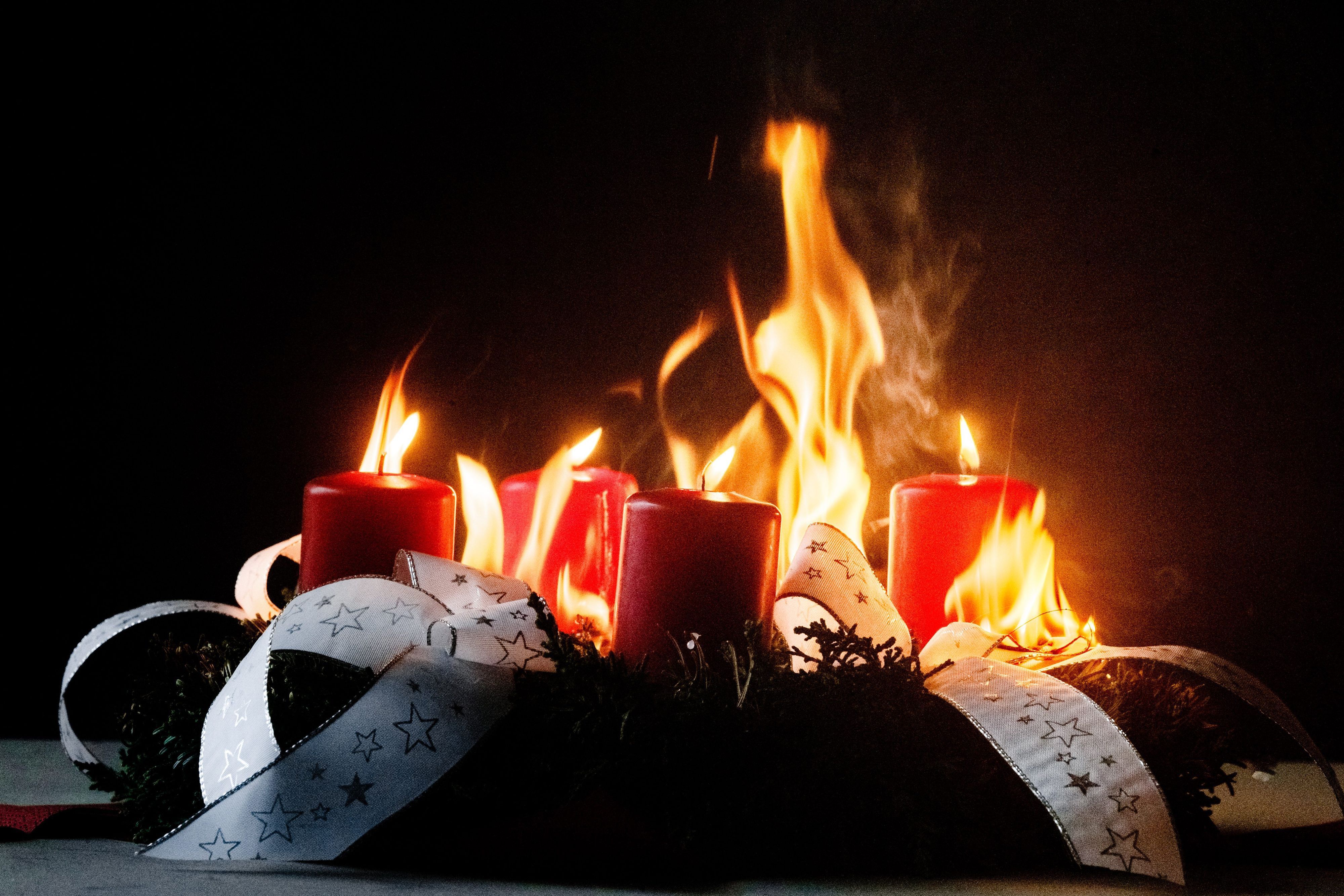 Ein Adventskranz mit vier roten Kerzen und weißem Band als Schleife steht in Flammen.