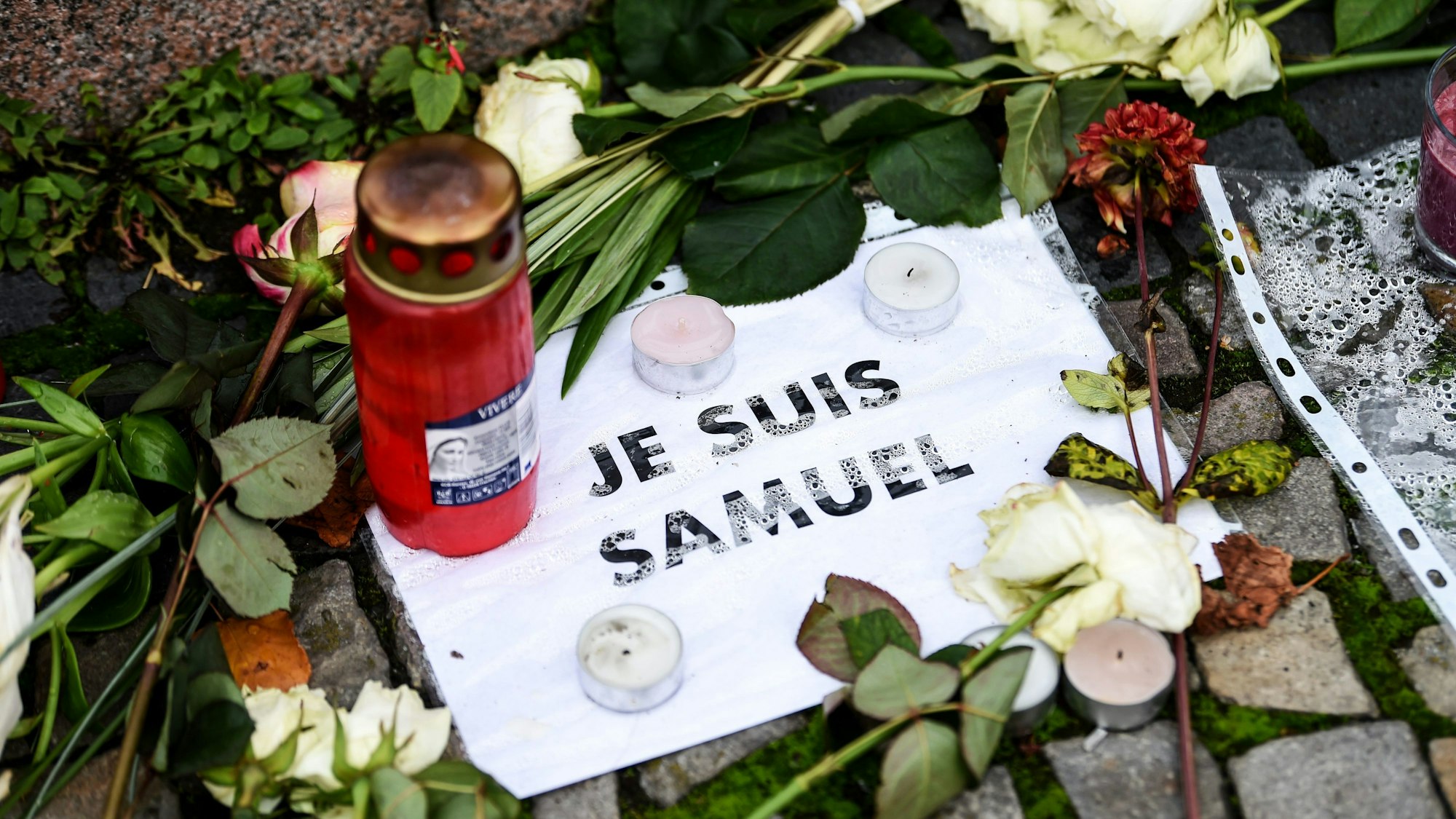 ARCHIV - 27.10.2020, Berlin: Vor der französischen Botschaft liegen Blumen, Kerzen und ein Blatt mit der Aufschrift ·Je suis Samuel·. In einem Pariser Vorort wurde der Lehrer Samuel Paty auf der Straße von einem mutmaßlichen Islamisten ermordet. (zu dpa " Urteile im Prozess um Ermordung von Lehrer Paty in Paris erwartet") Foto: Kira Hofmann/dpa-Zentralbild/dpa +++ dpa-Bildfunk +++