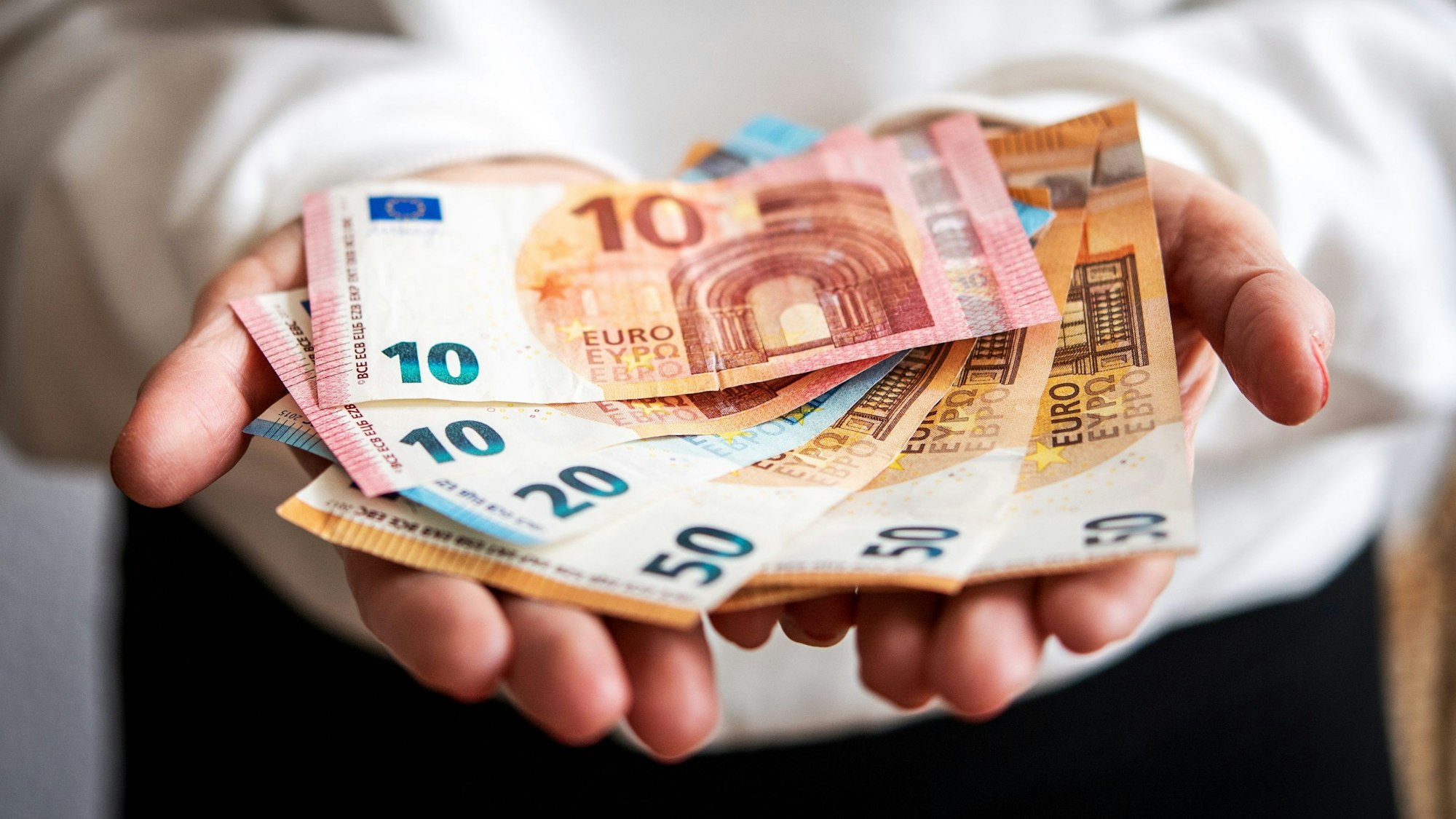 Zwei Hände reichen einen Stapel Euroscheine.