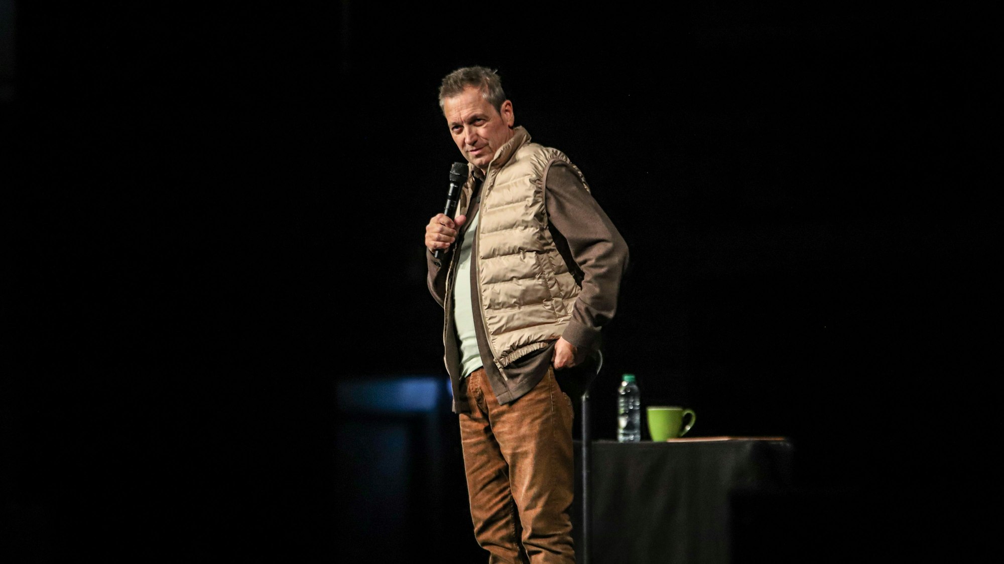 Dieter Nuhr steht auf einer dunklen Bühne.