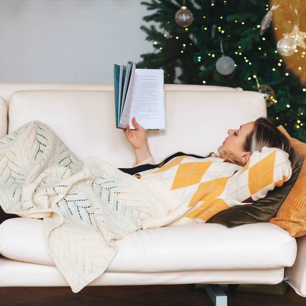Eine Frau liest, während sie auf dem Sofa im Wohnzimmer mit geschmücktem Weihnachtsbaum liegt