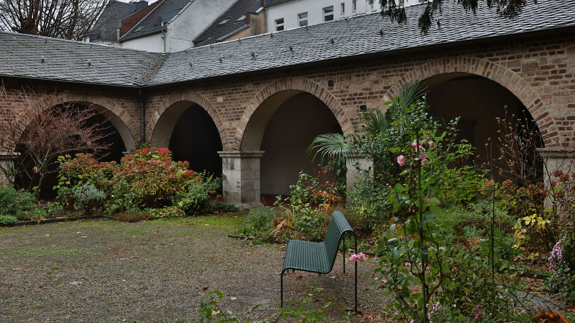 Zu sehen ist der Innenhof eines Klosters mit Pflanzen und einer grünen Sitzbank.