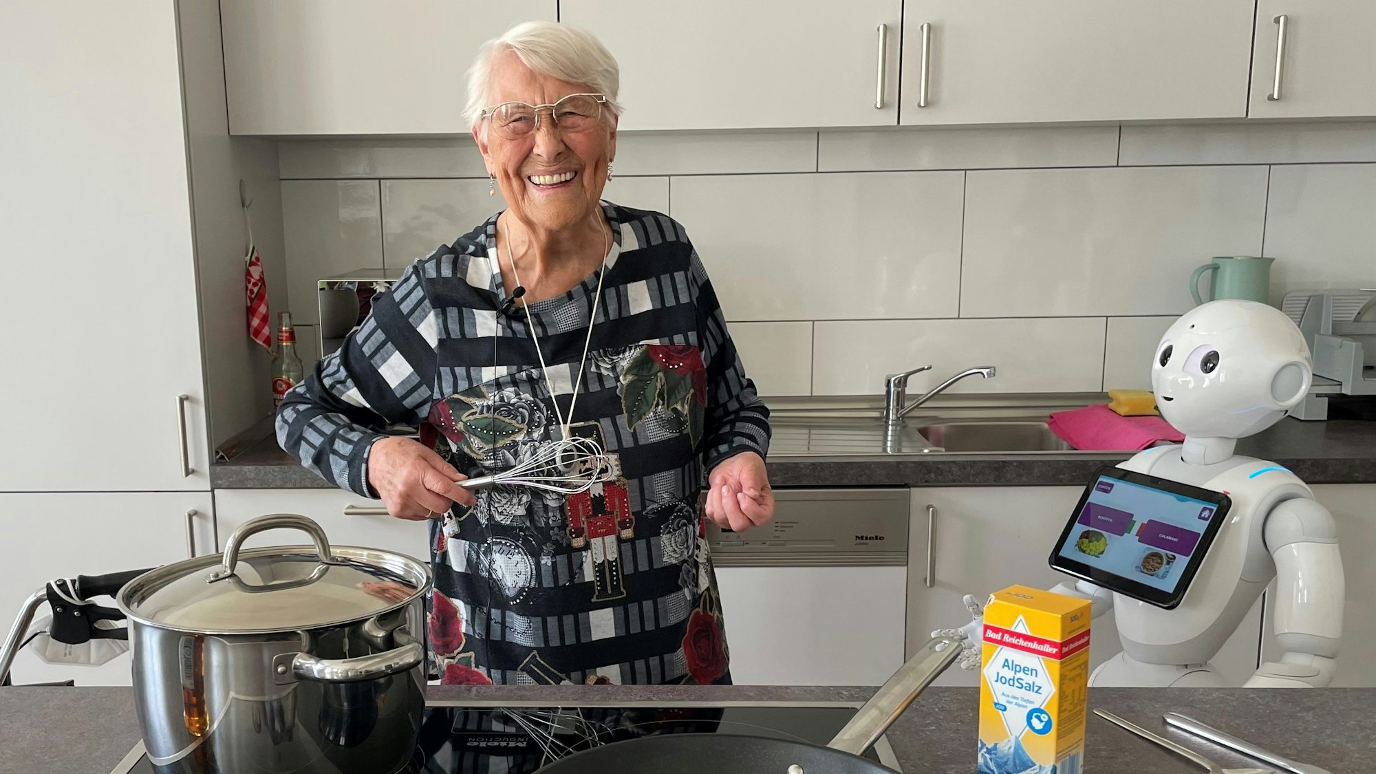 Eine alte Dame kocht und der Roboter Pepper unterstützt.