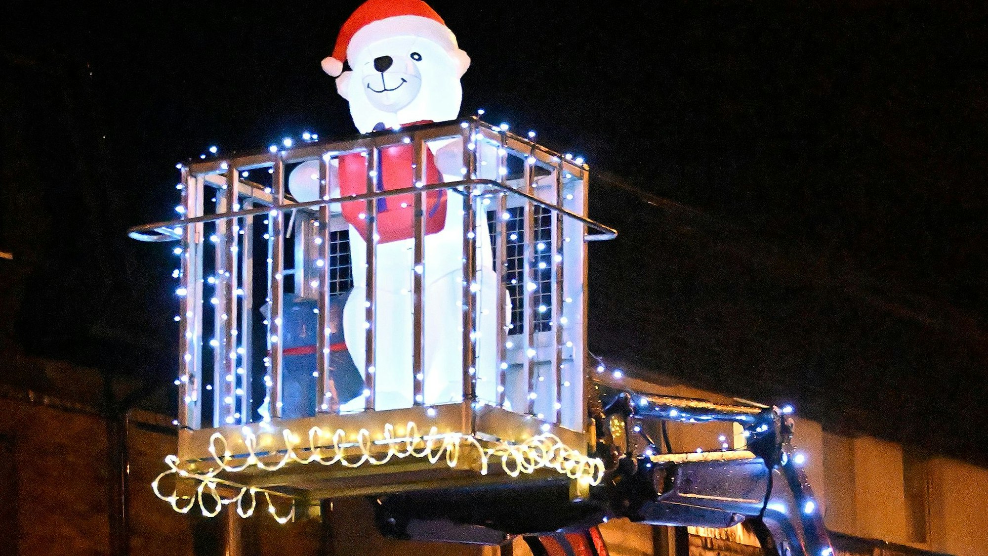 Ein leuchtender Schneemann steht in einer Box auf der Frontgabel eines Traktors.