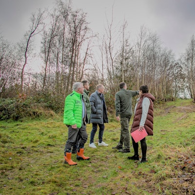 Mehrere Menschen stehen auf einer von dünnen Bäumen eingefassten Wiese.
