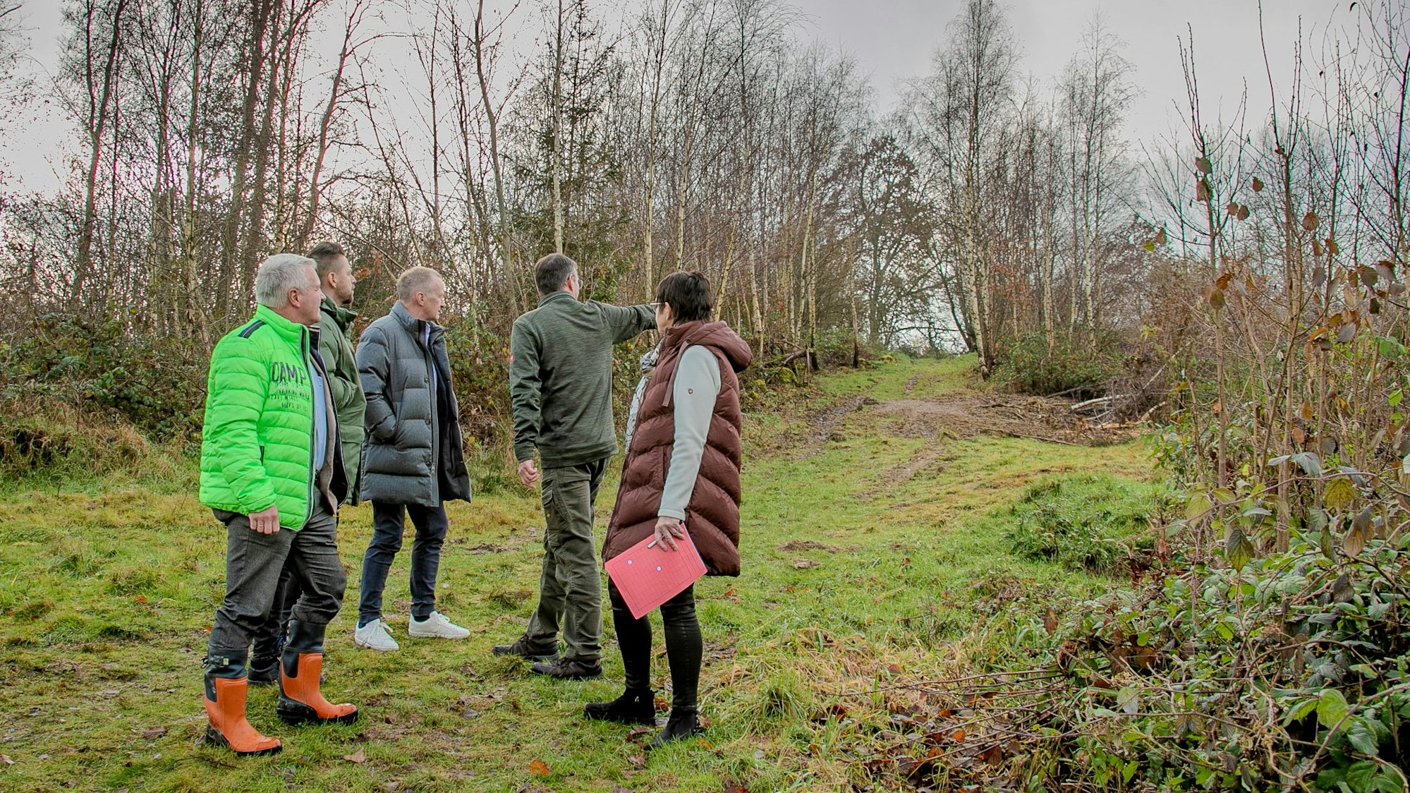 Mehrere Menschen stehen auf einer von dünnen Bäumen eingefassten Wiese.