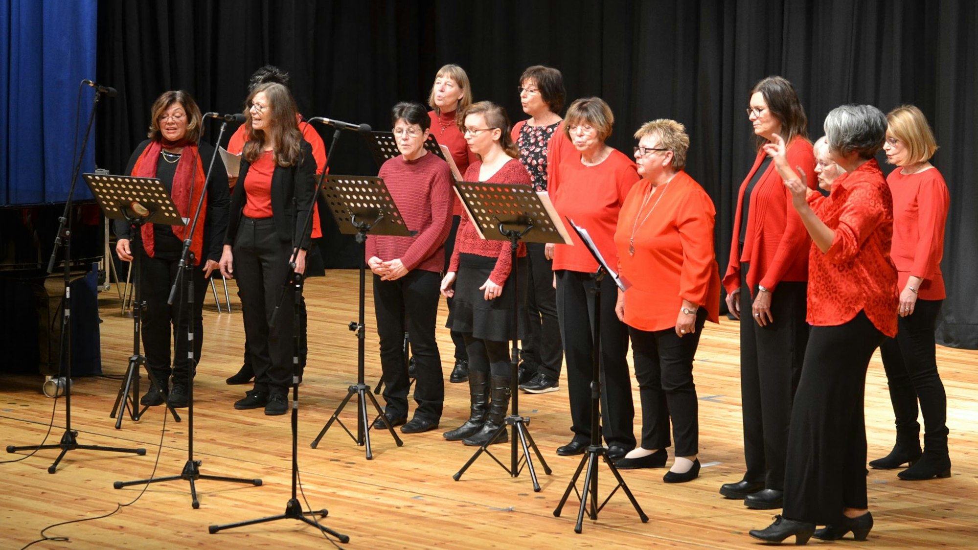 13 Frauen des Gospelchors „Go(o)d Sounds“ stehen in rot und schwarz auf einer Bühne und singen.