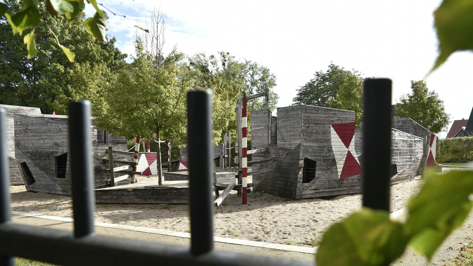 Hinter einem Zaun sind Spielgeräte aus Holz zu erkennen.