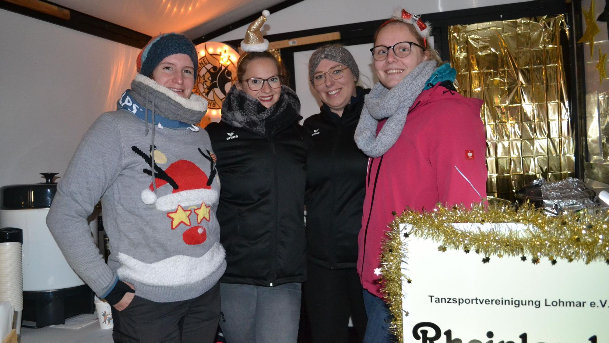 Vier junge Frauen an einem weihnachtlich dekoriertem Glühweinstand.
