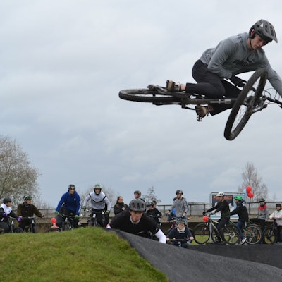 Ein Jugendlicher im grauen Sweatshirt führt einen Fahrrad-Trick in der Luft vor.