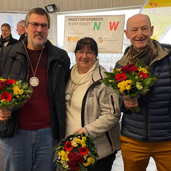 Eine Frau und zwei Männer halten Blumensträuße in den Händen.