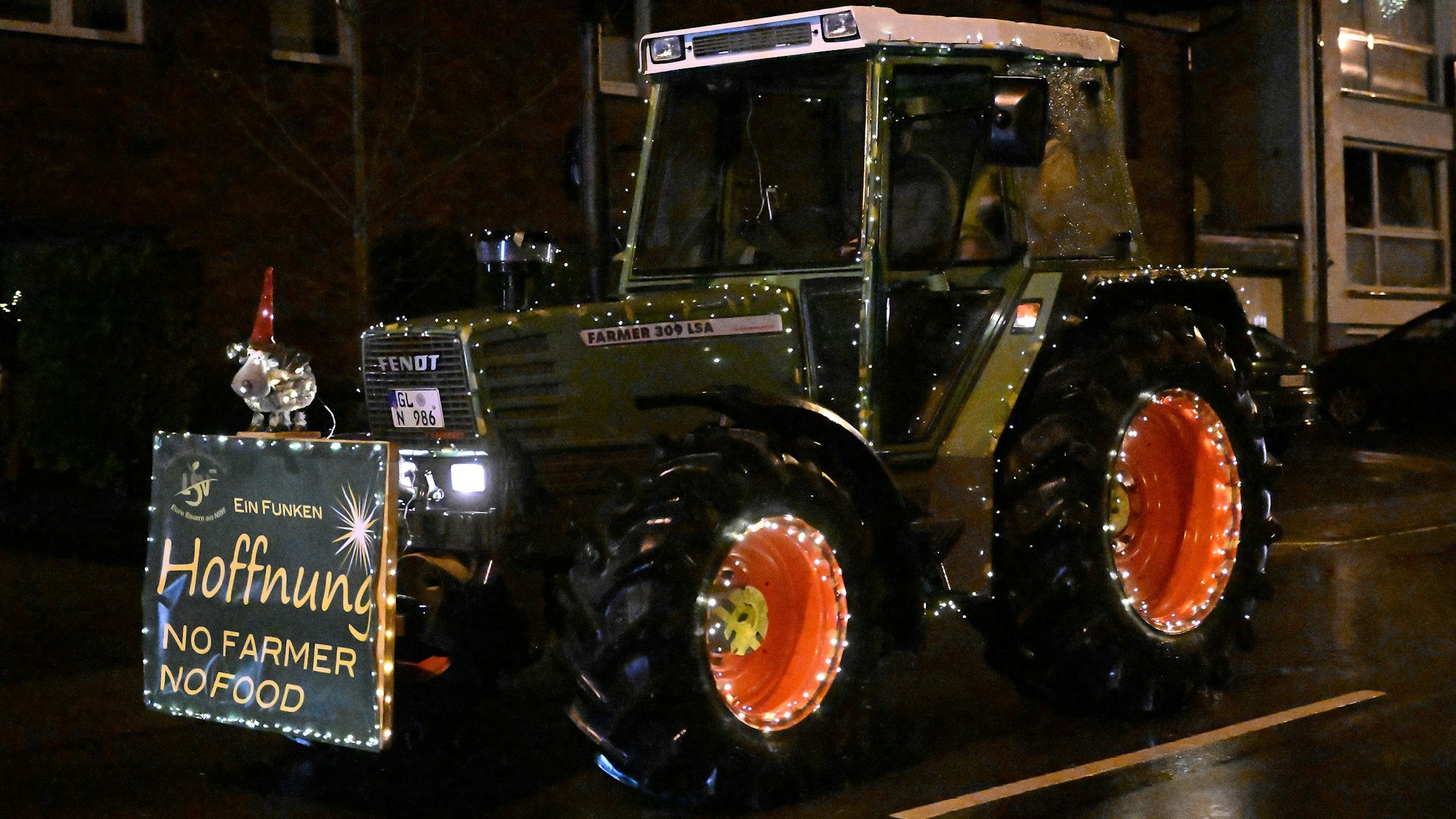 Eine Traktor mit einem beleuchteten Schild fährt über eine verregnete Straße.