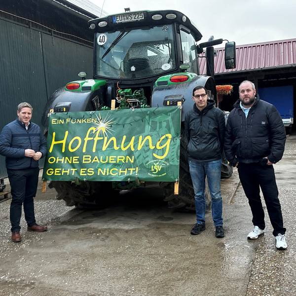 Das Foto zeigt die Landwirte und Landrat Markus Ramers neben einem Traktor, an dem ein Plakat mit der Aufschrift „Ein Funken Hoffnung. Ohne Bauern geht es nicht“ befestigt ist.