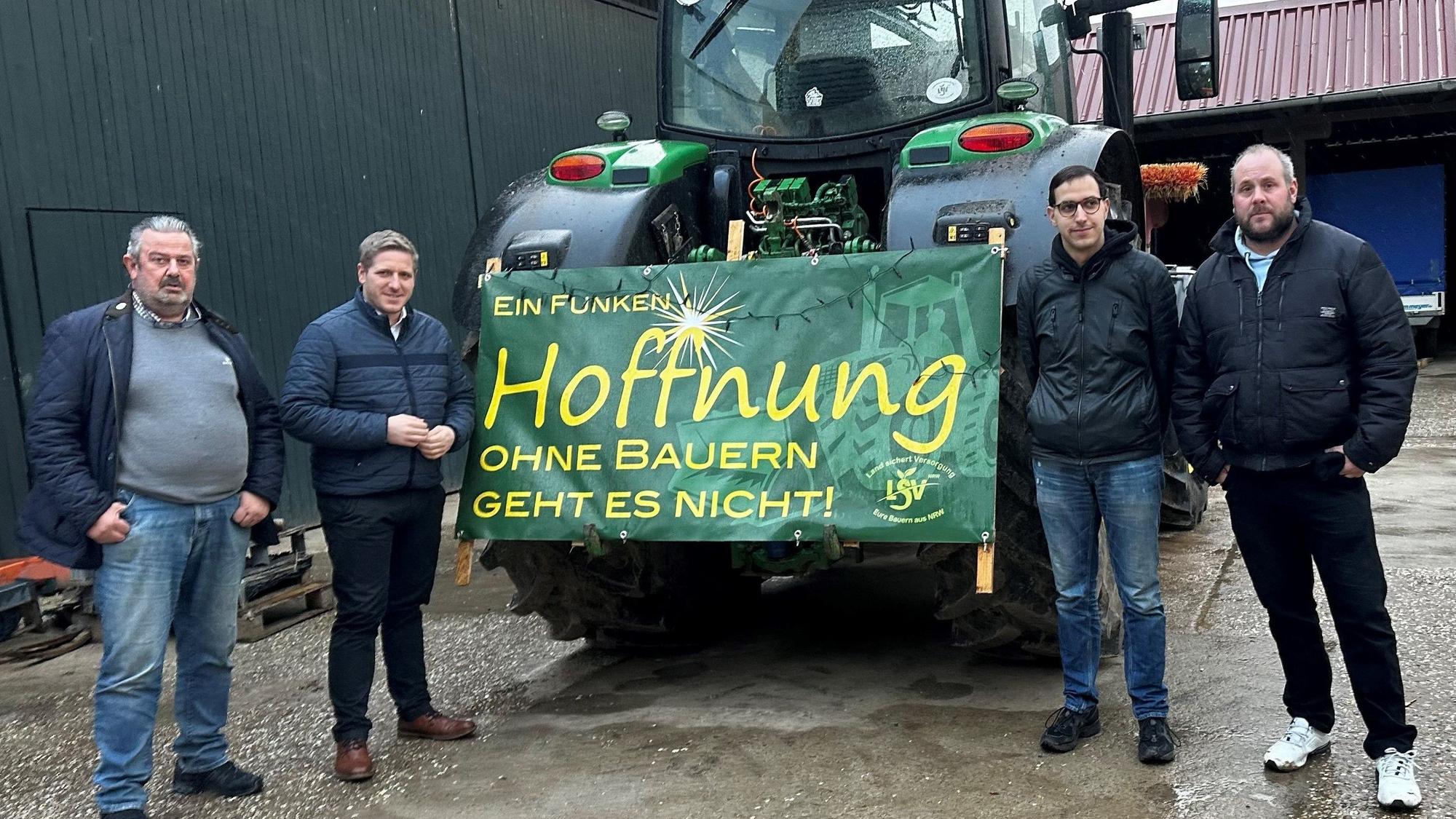 Das Foto zeigt die Landwirte und Landrat Markus Ramers neben einem Traktor, an dem ein Plakat mit der Aufschrift „Ein Funken Hoffnung. Ohne Bauern geht es nicht“ befestigt ist.
