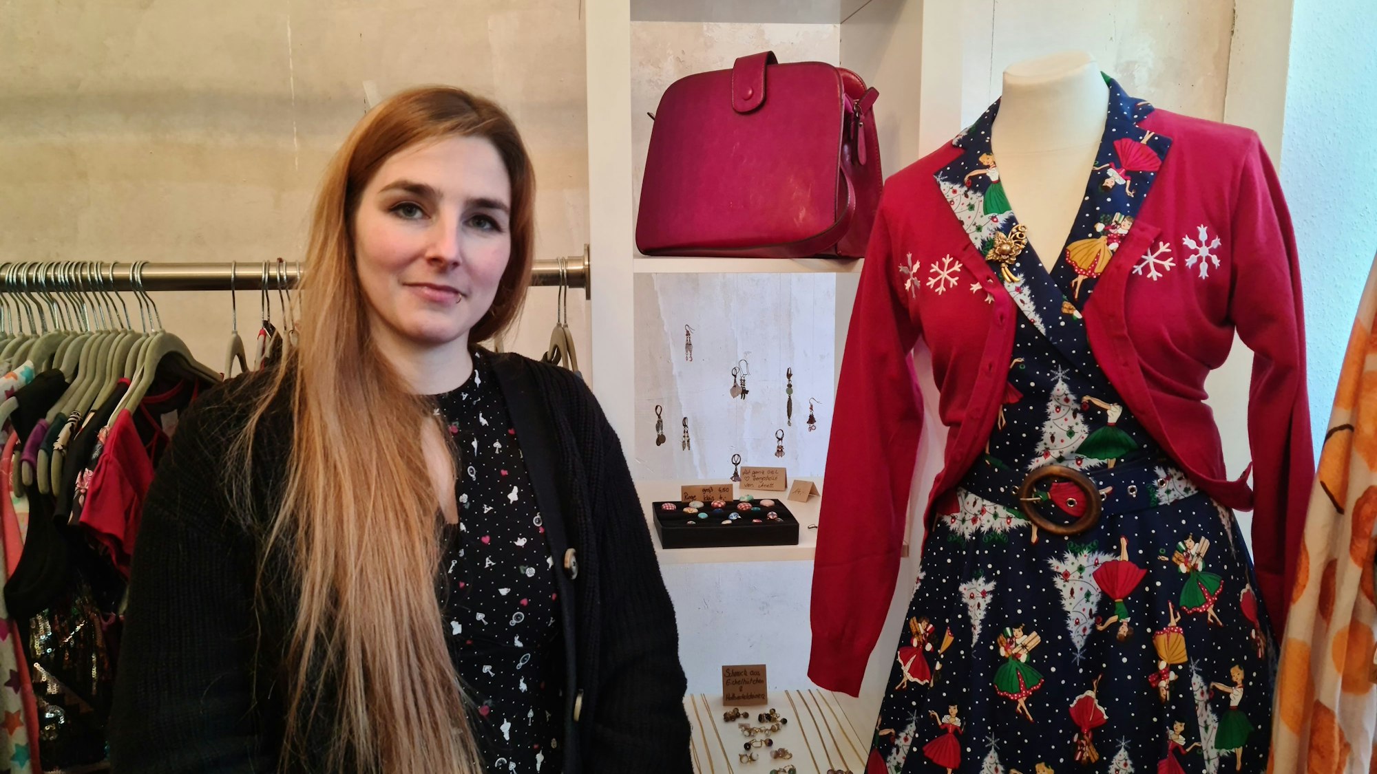Sandra Kahr, Inhaberin der Boutique Kahrla, vor einer Kleiderstange mit bunten Anziehsachen und einem Regal mit Handtasche und Schmuck.