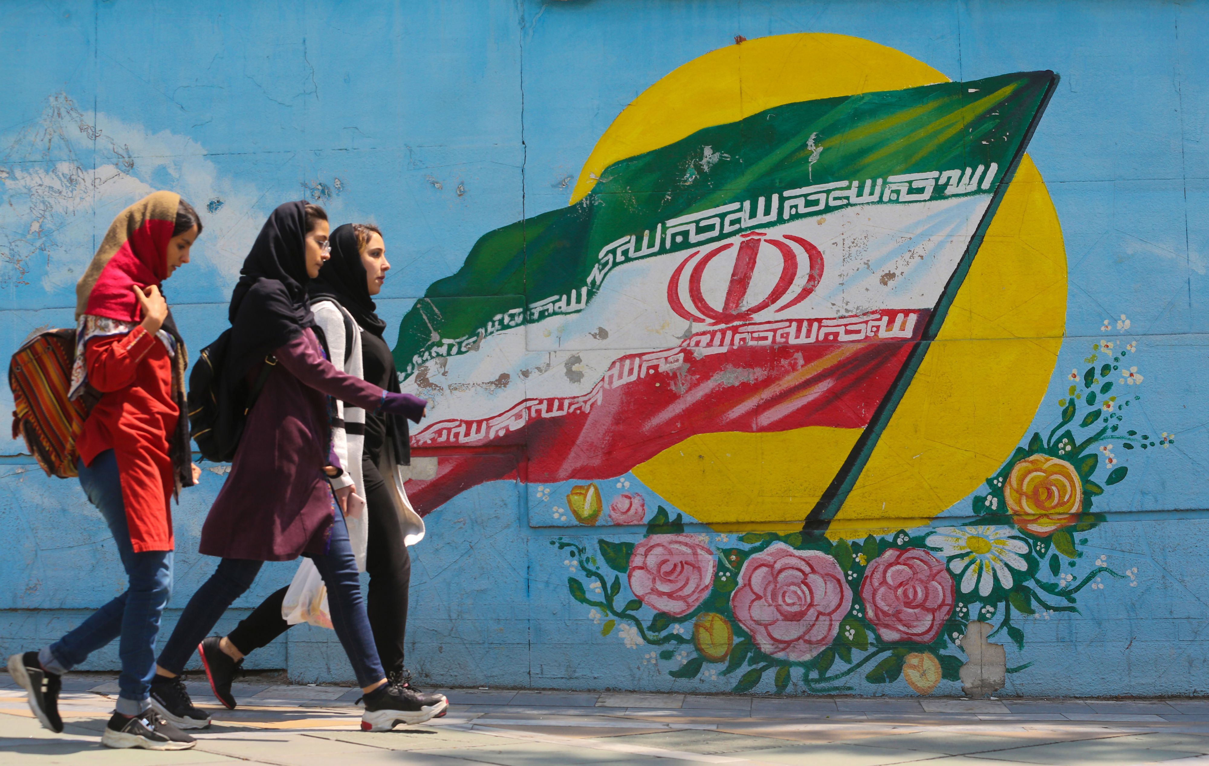 Junge Mädchen laufen vor einem Wandgemälde mit der iranischen Nationalflagge im Zentrum der Hauptstadt Teheran.