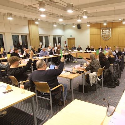 Männer und Frauen in einem Sitzungssaal bei einer Abstimmung.