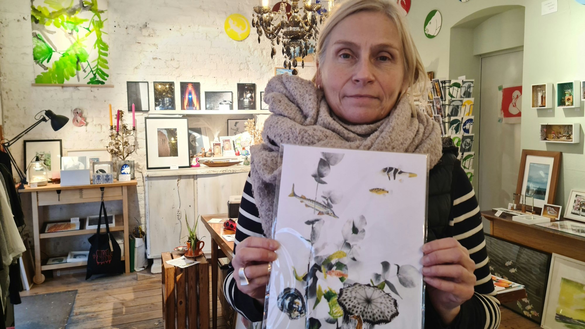 Eine Frau mit Schal hält ein buntes Bild hoch