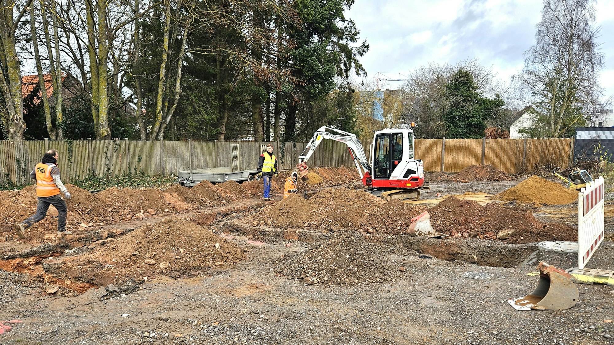 Arbeiter ziehen mit Hilfe eines Baggers Gräben für die Versorgungsleitungen.