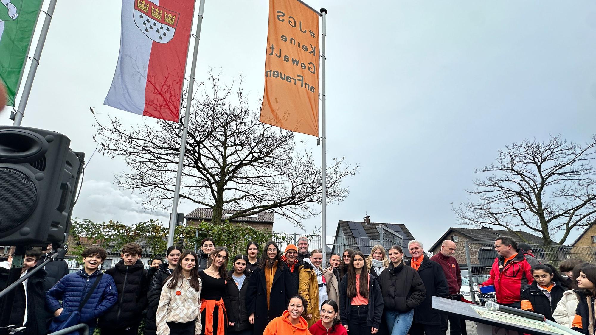 Gruppenfoto mit Schülern und Bezirksbürgermeister Manfred Giesen, die orangene Fahne und die mit dem Kölner Wappen im Hintergrund zu sehen.