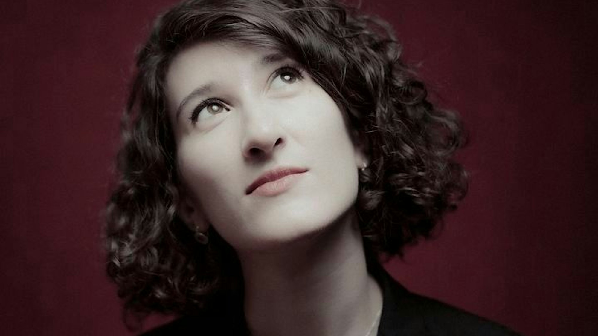 Das Bild zeigt das Gesicht der Pianistin Nathalia Milstein. Sie hat braunes, lockiges Haar und trägt schwarze Kleidung.