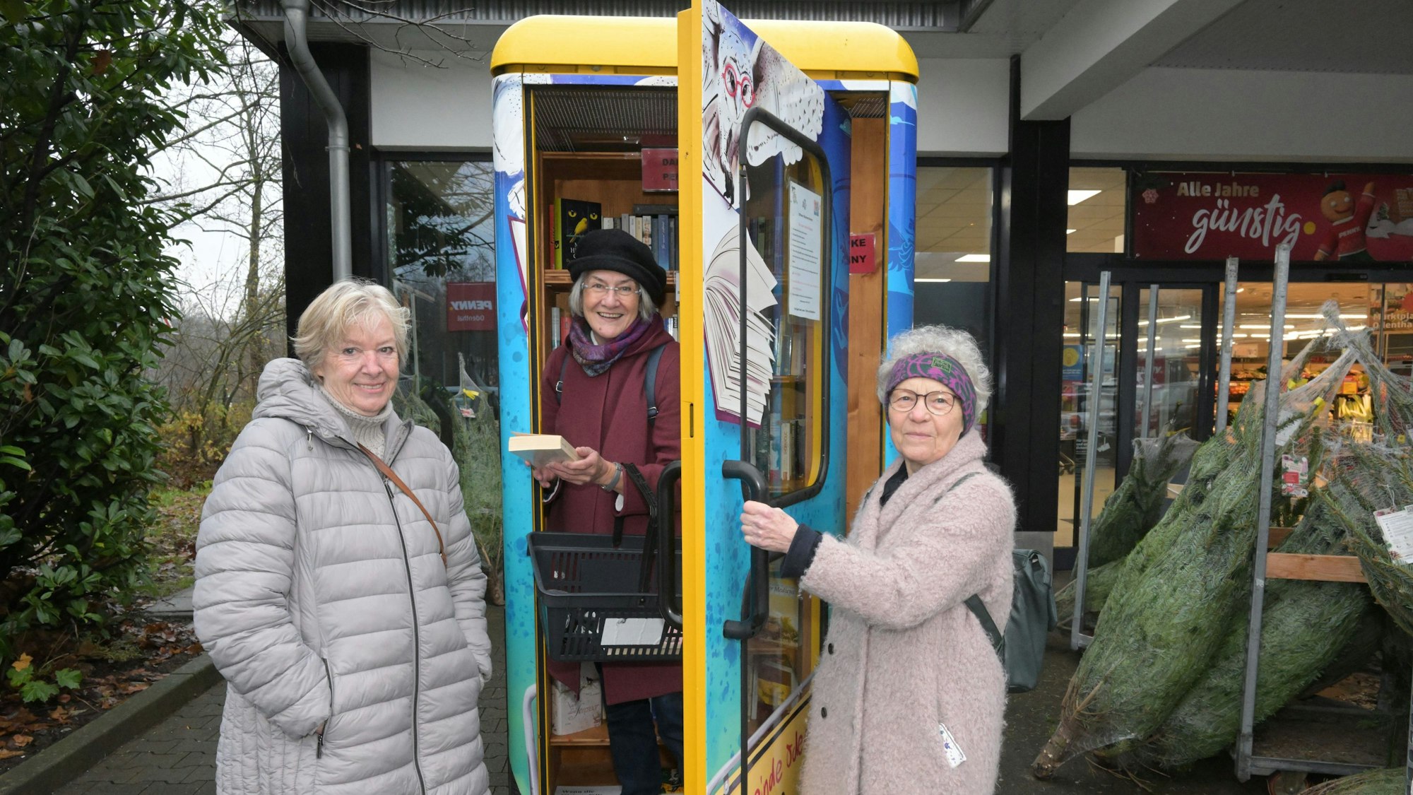 Ulrike Viering, Astrid Martini Hamann, Linde Tisbrummel (v.l.) stehen in Winterjacken in und teilweise im bunt bemalten Bücherschrank.