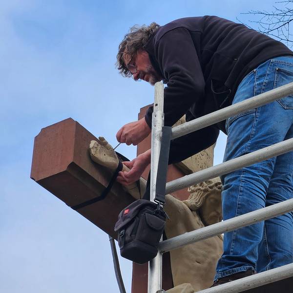 Ein Mann auf einem Gerüst arbeitet an einer steinernen Jesusfigur.