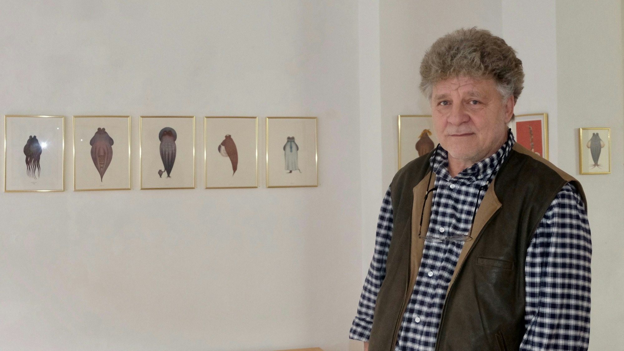 Ein Mann mit grauem Haar steht vor kleinformatigen Bildern mit Tintenfischen.