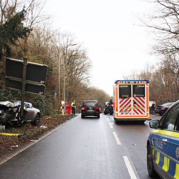 Ein völlig demoliertes Auto steht an einem abgeknickten Schildertafelmast. Auf der Straße stehen Rettungsdienst- und Polizeifahrzeuge.