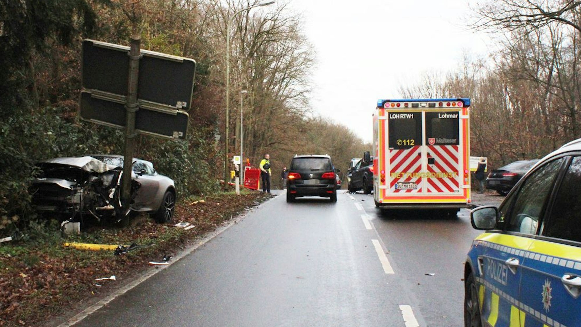 Ein völlig demoliertes Auto steht an einem abgeknickten Schildertafelmast. Auf der Straße stehen Rettungsdienst- und Polizeifahrzeuge.