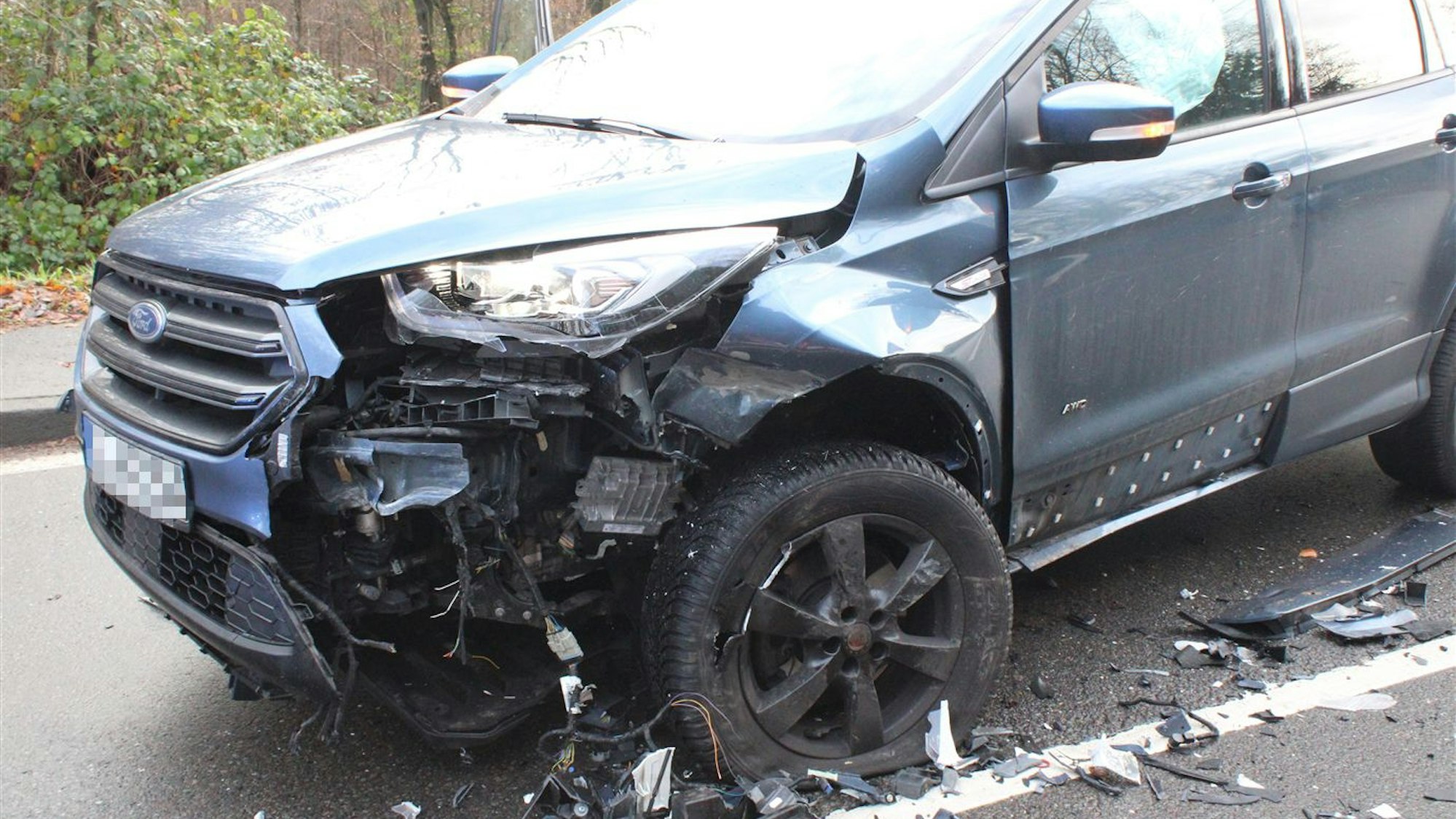 Ein Unfallwagen mit schwerem Schaden an der vorderen linken Ecke steht auf einer Straße.