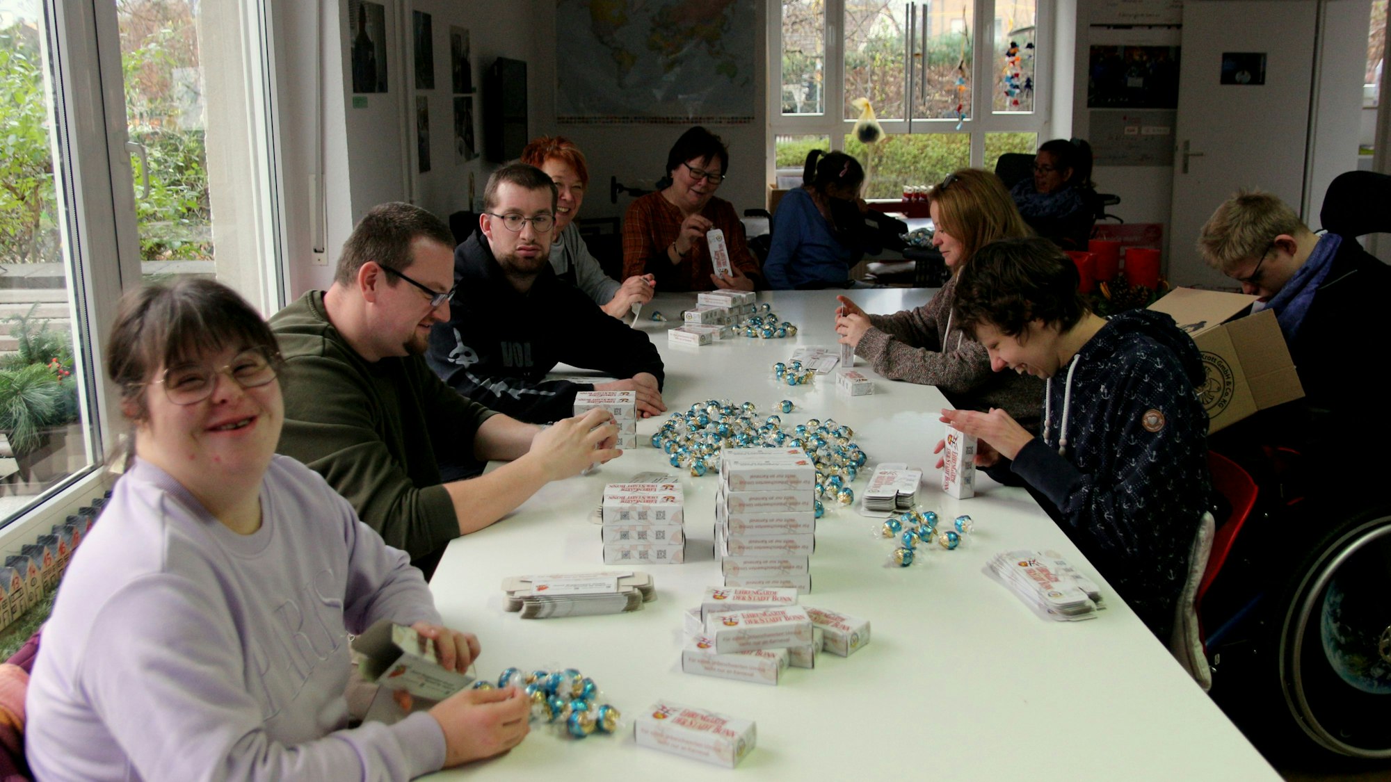 Junge Erwachsene sitzen an einem Tisch, sie verpacken Süßigkeiten.