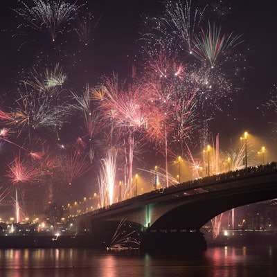 Die Kennedybrücke in Bonn an Silvester aus der Untenansicht mitsamt Rhein davor. Feuerwerk erleuchtet den dunklen Nachthimmel.