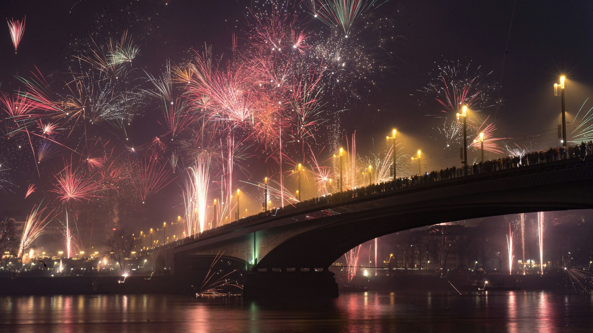 Die Kennedybrücke in Bonn an Silvester aus der Untenansicht mitsamt Rhein davor. Feuerwerk erleuchtet den dunklen Nachthimmel.