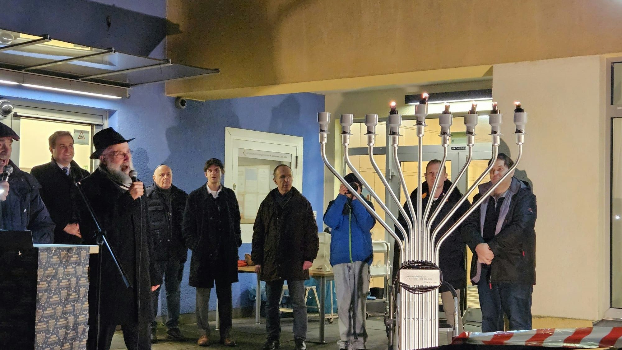 Menschen stehen vor einem Gebäude zusammen, in ihrer Mitte eine Chanukkia.