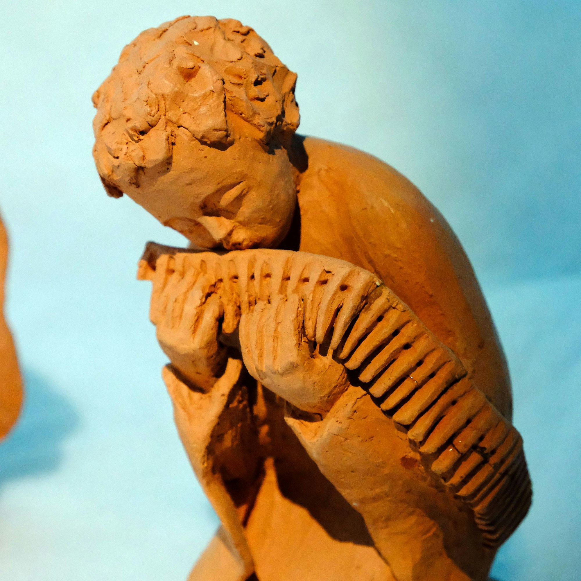 Detail der Krippe „Traum der Engel“: Eine tönerne Engelsfigur spielt Flöte auf einem Patronengurt.