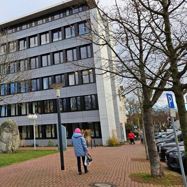 Eine Frau geht auf ein mehrstöckiges graues Bürogebäude zu.