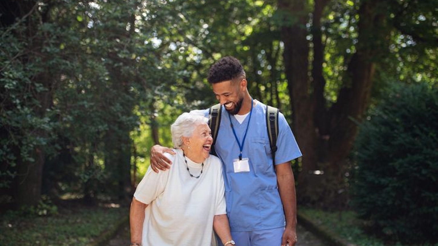 Caregiver man with shopping bag taking senior woman with walker for a walk to shop.