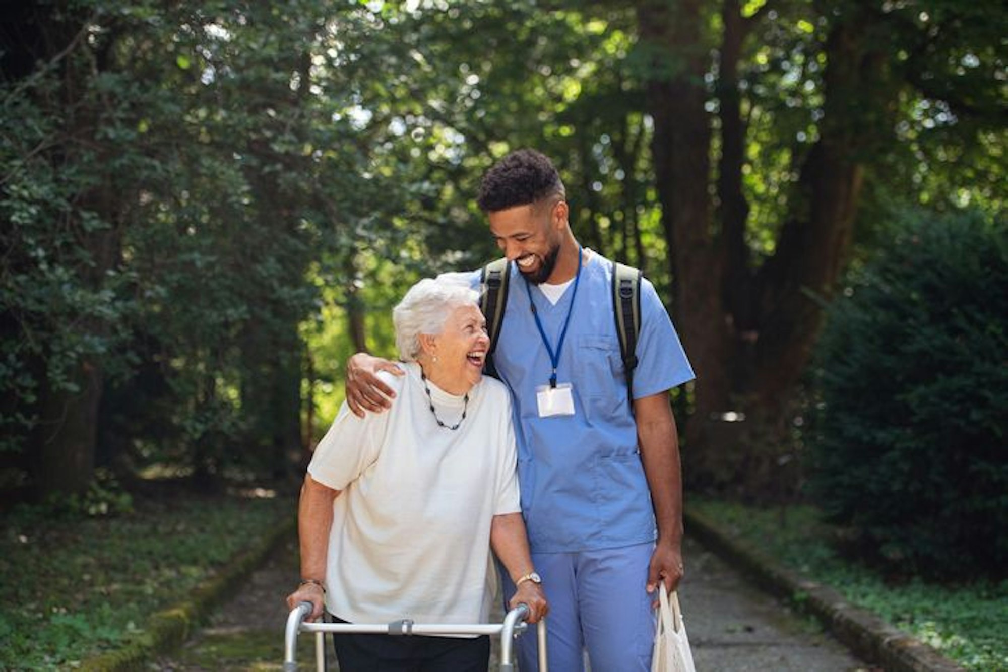 Caregiver man with shopping bag taking senior woman with walker for a walk to shop.