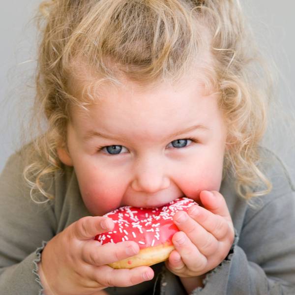 Ein kleines Mädchen isst einen pinken Donut. Symbolbild