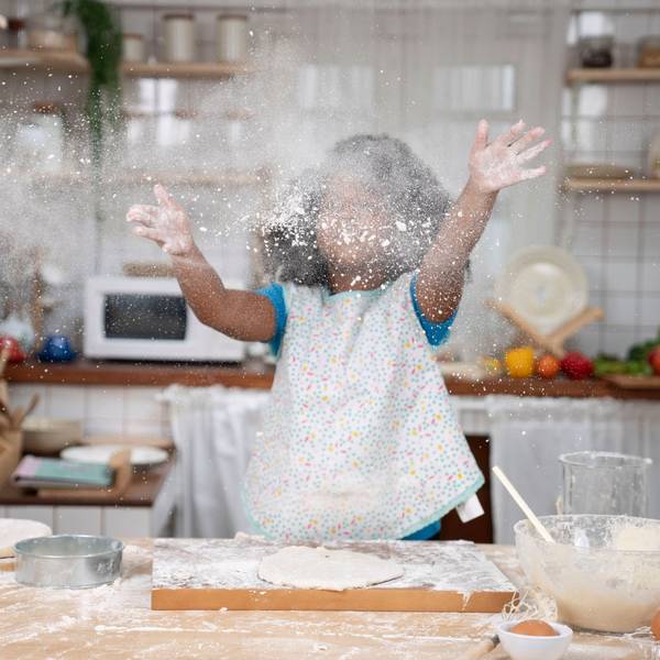 Ein kleines Mädchen wirft beim Backen Mehl in die Luft.