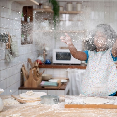 Ein kleines Mädchen wirft beim Backen Mehl in die Luft.